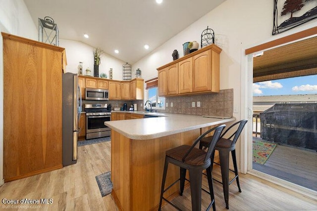 4411 N Campbell Rd, Otis Orchards, WA 99027 - kitchen featuring appliances with stainless steel finishes, a peninsula, light wood finished floors, a sink, and vaulted ceiling