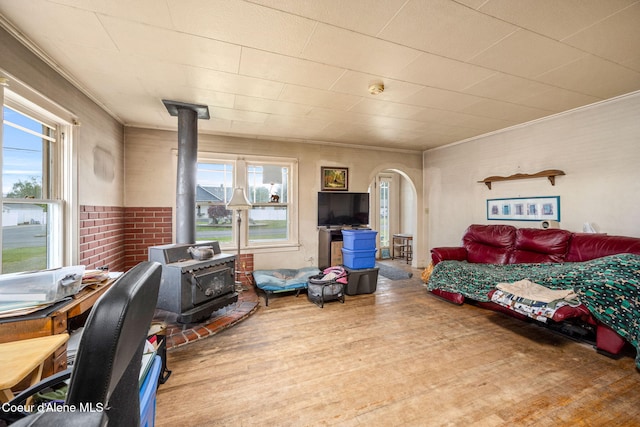 living area with a wood stove, healthy amount of natural light, wood finished floors, arched walkways, and ornamental molding