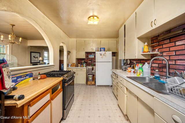 kitchen featuring freestanding refrigerator, gas stove, light flooring, light countertops, and a chandelier