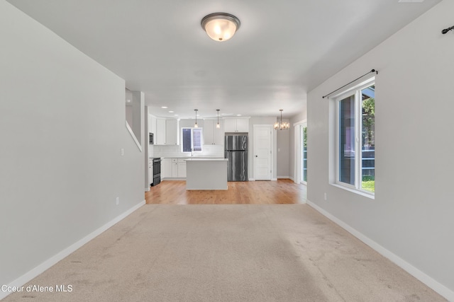 161 White Way, Priest River, ID 83856 - unfurnished living room with light colored carpet, a chandelier, baseboards, and plenty of natural light