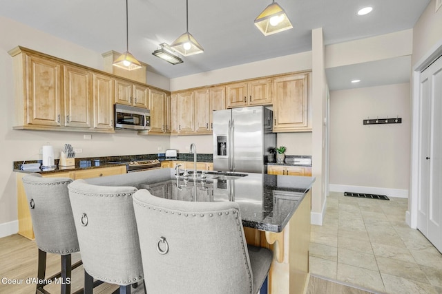kitchen with stainless steel appliances, light brown cabinets, a breakfast bar area, a sink, and baseboards