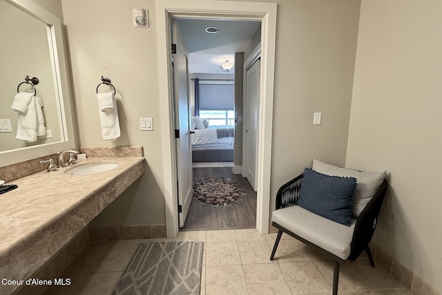 ensuite bathroom featuring a sink, tile patterned floors, and baseboards