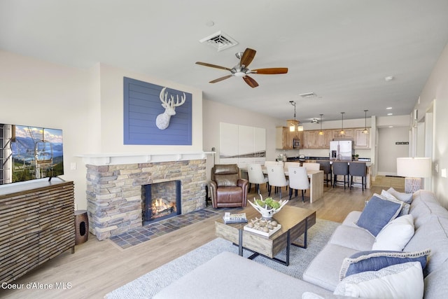 living area featuring light wood-type flooring, a ceiling fan, and a stone fireplace