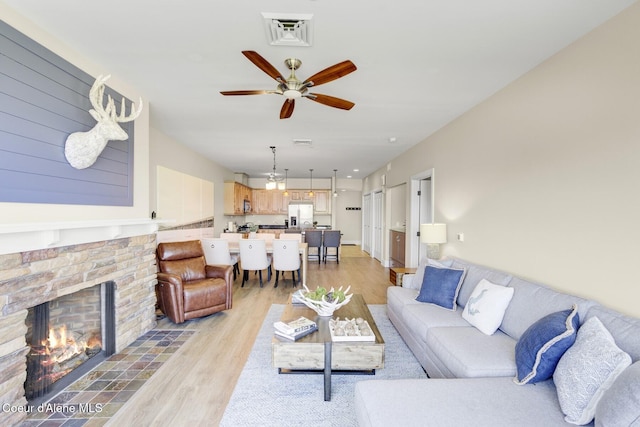 living area with light wood-type flooring, a stone fireplace, and a ceiling fan