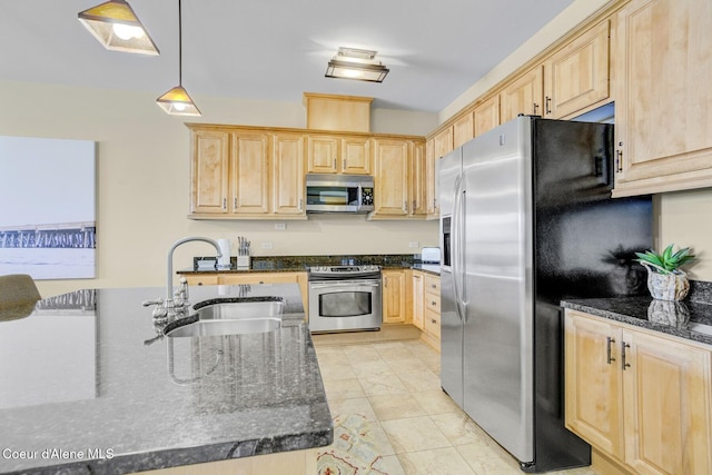 kitchen featuring light brown cabinetry, stainless steel appliances, a sink, dark stone counters, and hanging light fixtures