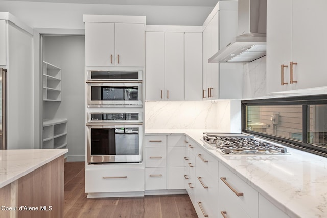 2867 W Lumber Ln, Coeur Dalene, ID 83814 - kitchen featuring wall chimney range hood, appliances with stainless steel finishes, backsplash, light stone counters, and light wood-style floors
