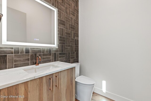 2867 W Lumber Ln, Coeur Dalene, ID 83814 - half bathroom featuring vanity, toilet, tasteful backsplash, and wood finished floors