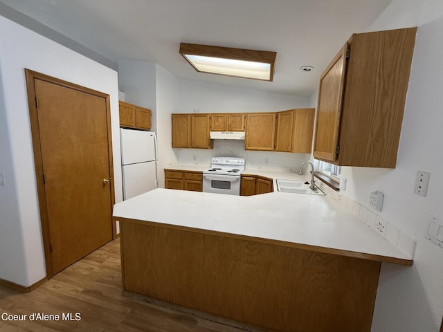 5188 E Woodland Dr, Post Falls, ID 83854 - kitchen featuring white appliances, under cabinet range hood, vaulted ceiling, brown cabinets, and a peninsula