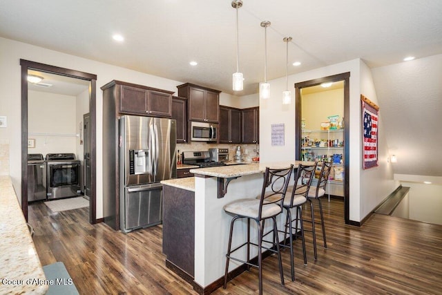 4631 E Alopex Ln, Post Falls, ID 83854 - kitchen featuring appliances with stainless steel finishes, washer and dryer, dark brown cabinetry, dark wood-type flooring, and a breakfast bar area