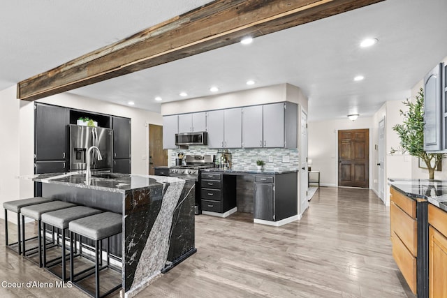 kitchen with appliances with stainless steel finishes, a sink, dark stone countertops, light wood finished floors, and recessed lighting