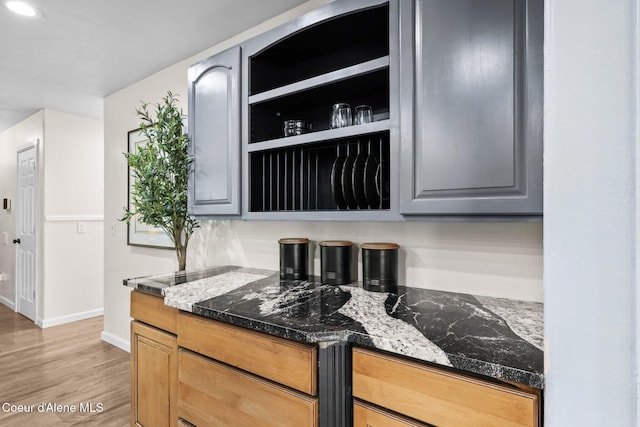 kitchen featuring baseboards, light wood finished floors, gray cabinets, dark stone countertops, and recessed lighting