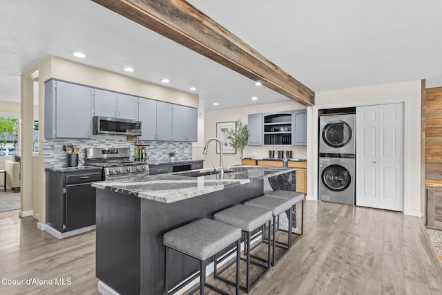 kitchen with appliances with stainless steel finishes, stacked washer / drying machine, a sink, open shelves, and stone counters
