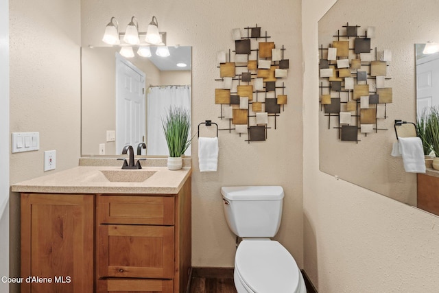 full bathroom featuring toilet, vanity, and a textured wall