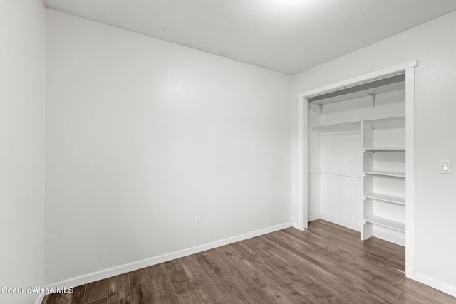 unfurnished bedroom with dark wood-style flooring, baseboards, and a closet