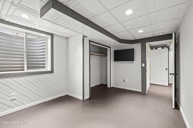 unfurnished bedroom with baseboards, recessed lighting, concrete floors, a closet, and wooden walls