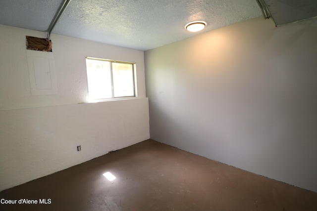 empty room featuring concrete flooring, electric panel, and a textured ceiling