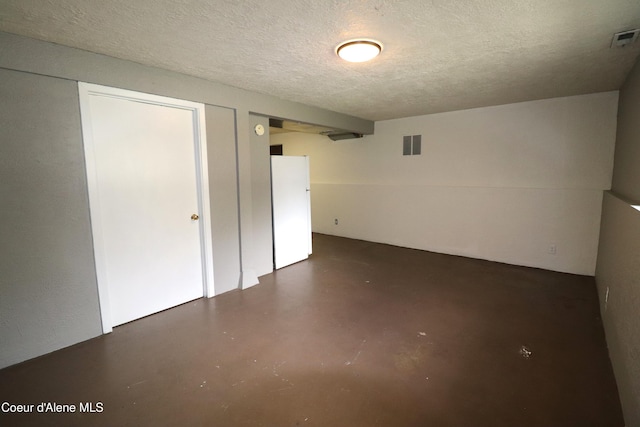 finished below grade area featuring freestanding refrigerator and a textured ceiling