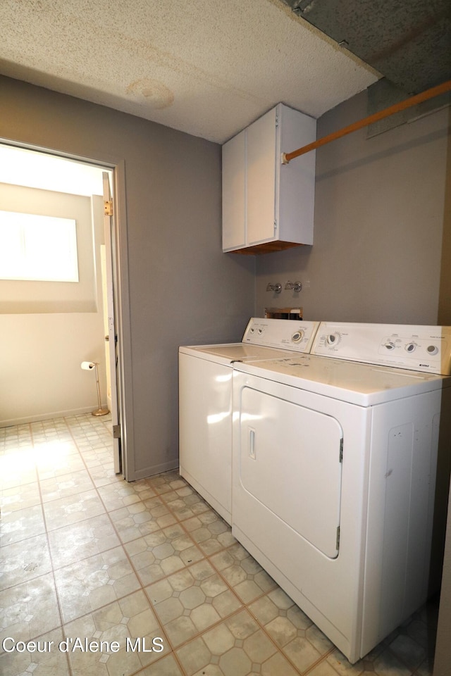 washroom featuring separate washer and dryer, cabinet space, a textured ceiling, light flooring, and baseboards