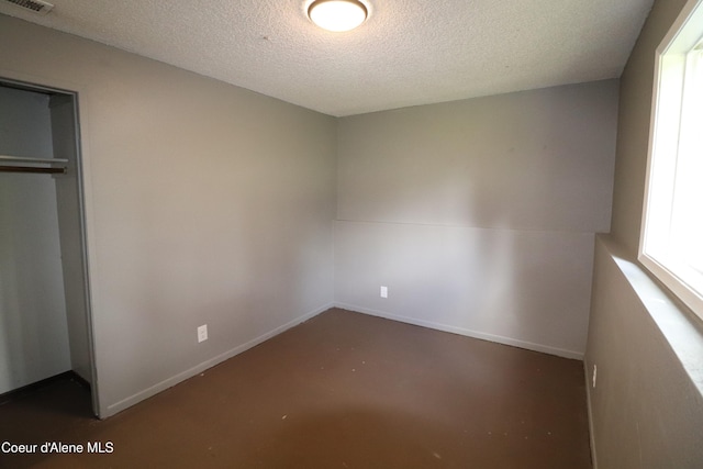 unfurnished bedroom featuring a textured ceiling, a closet, baseboards, and concrete floors