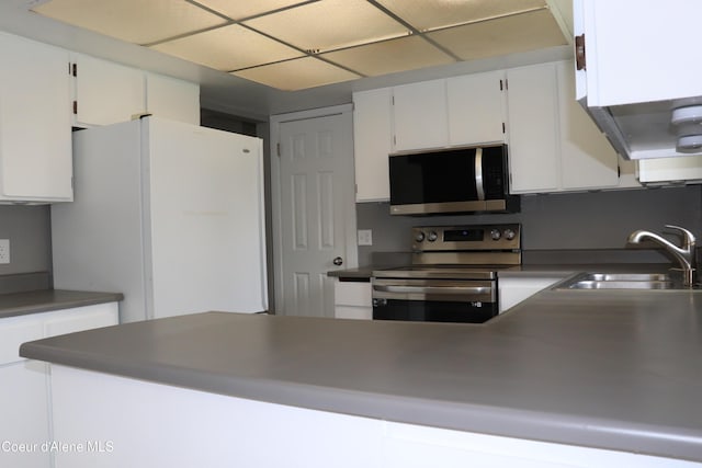 kitchen featuring stainless steel appliances, a sink, white cabinetry, dark countertops, and a peninsula