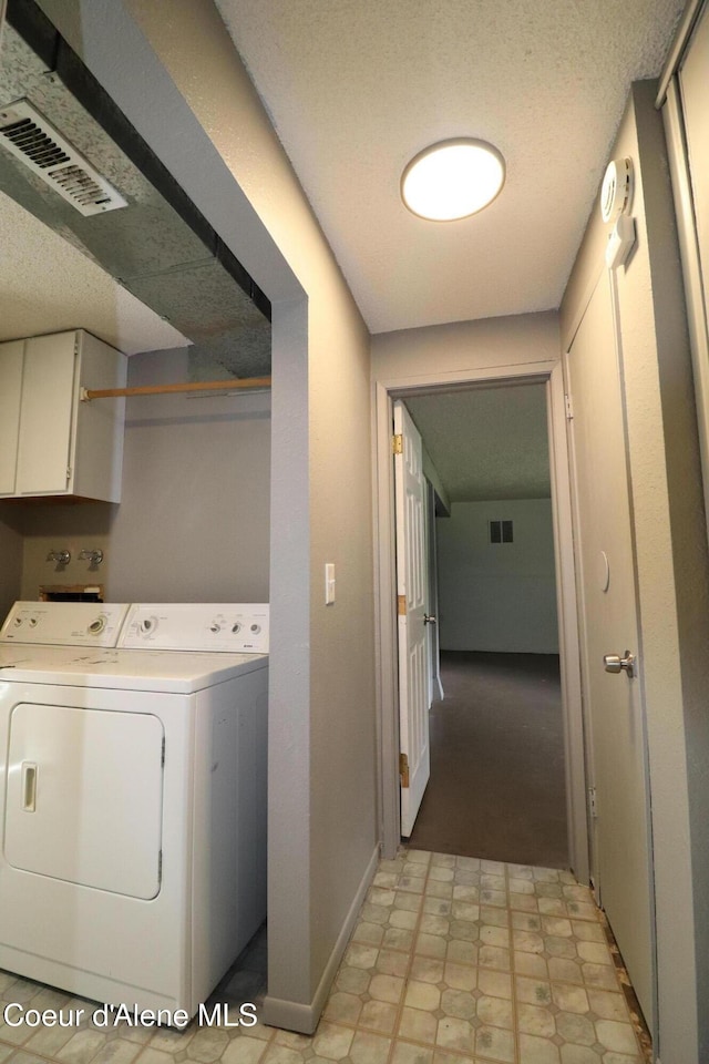 laundry area featuring cabinet space, washer and clothes dryer, a textured ceiling, and baseboards