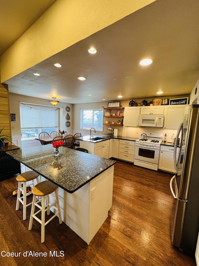 8351 N Audubon Dr, Hayden, ID 83835 - kitchen with white appliances, a sink, dark wood-style flooring, white cabinets, and a breakfast bar area