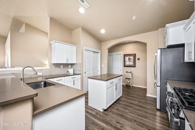 kitchen with a sink, lofted ceiling, a kitchen island, arched walkways, and stainless steel range with gas cooktop