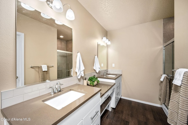 full bath featuring a shower stall, wood finished floors, double vanity, and decorative backsplash