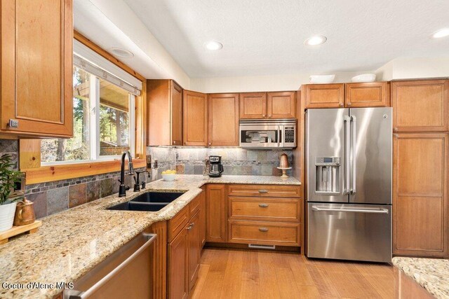 kitchen featuring appliances with stainless steel finishes, a sink, brown cabinets, decorative backsplash, and light wood-style flooring