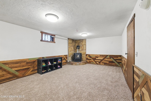 6699 Colburn Culver Rd, Sandpoint, ID 83864 - living area featuring a wood stove, carpet flooring, a textured ceiling, wainscoting, and wood walls