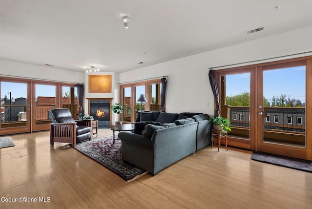 living room with french doors, light wood-style flooring, and a glass covered fireplace