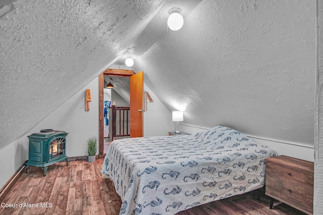 bedroom featuring a wood stove, a textured ceiling, wood finished floors, baseboards, and lofted ceiling