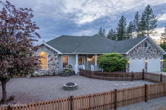 684 Chute Canyon Way, Bonners Ferry, ID 83805 - view of front of property with stone siding, a fire pit, a porch, a garage, and a shingled roof