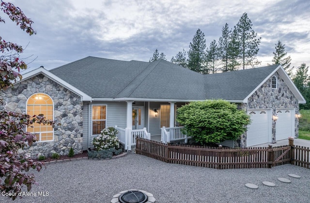 684 Chute Canyon Way, Bonners Ferry, ID 83805 - view of front of house featuring stone siding, covered porch, a garage, roof with shingles, and fence