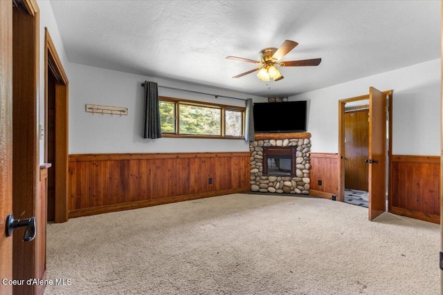 5239 E Dodd Rd, Hayden, ID 83835 - unfurnished living room featuring wainscoting, wood walls, ceiling fan, carpet, and a stone fireplace