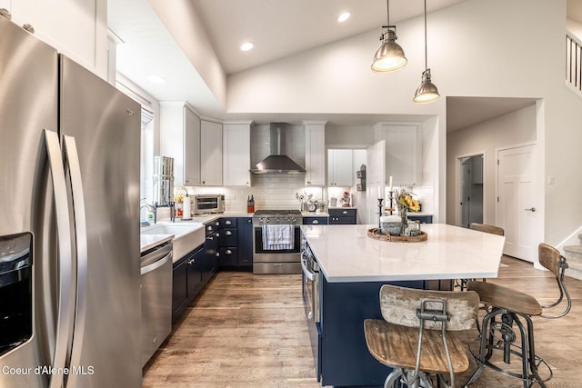 1769 N Chetco Dr, Post Falls, ID 83854 - kitchen featuring appliances with stainless steel finishes, wall chimney exhaust hood, a kitchen breakfast bar, a kitchen island, and light wood-style flooring