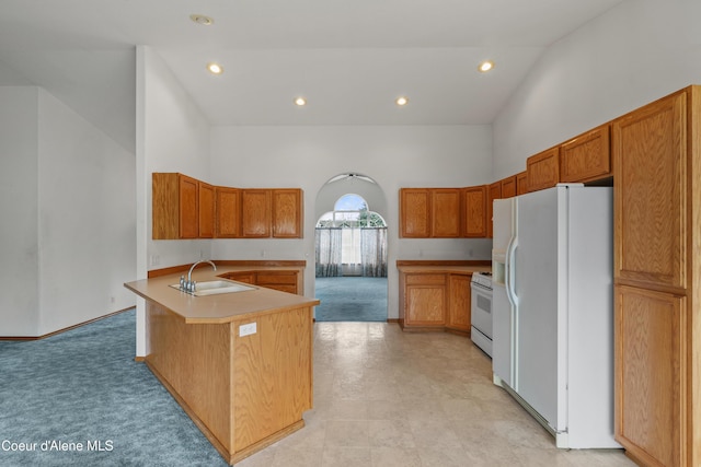 kitchen featuring white appliances, a sink, a peninsula, a high ceiling, and brown cabinets