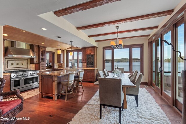 dining room featuring dark wood-type flooring, a water view, beamed ceiling, recessed lighting, and a chandelier
