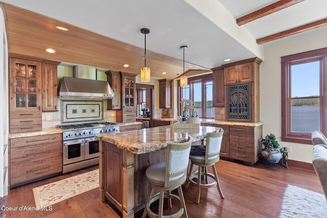 kitchen featuring range with two ovens, wall chimney range hood, a center island, glass insert cabinets, and backsplash