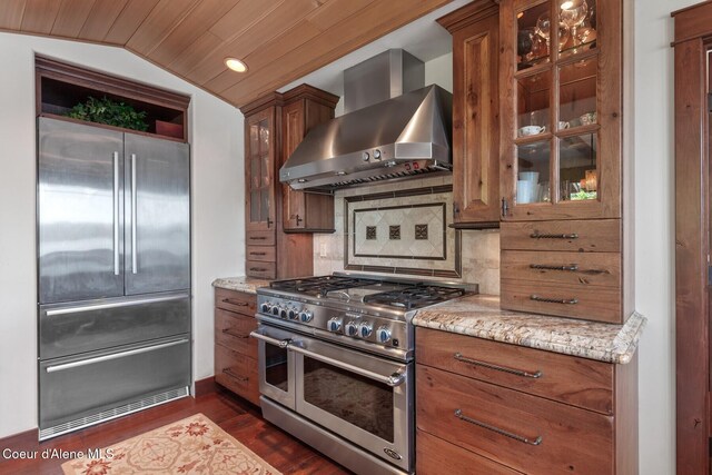 kitchen featuring high end appliances, wall chimney exhaust hood, light stone counters, backsplash, and vaulted ceiling