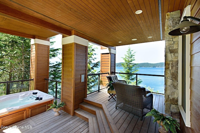 balcony with an outdoor hot tub and a water view