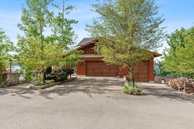 view of property hidden behind natural elements with asphalt driveway and fence