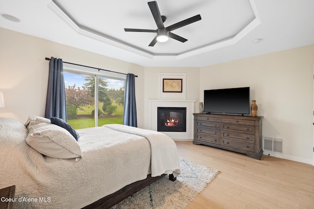22385 N Ranch View Dr, Rathdrum, ID 83858 - bedroom featuring a tray ceiling, a glass covered fireplace, light wood-style floors, a ceiling fan, and baseboards