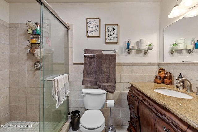 bathroom with wainscoting, a stall shower, vanity, toilet, and tile walls