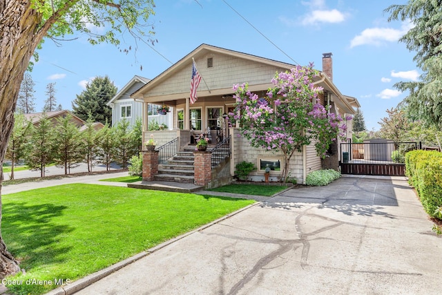 view of front of home with a front lawn, a chimney, covered porch, stairway, and concrete driveway