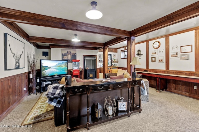 carpeted living room featuring beamed ceiling, a wainscoted wall, wooden walls, and ornamental molding