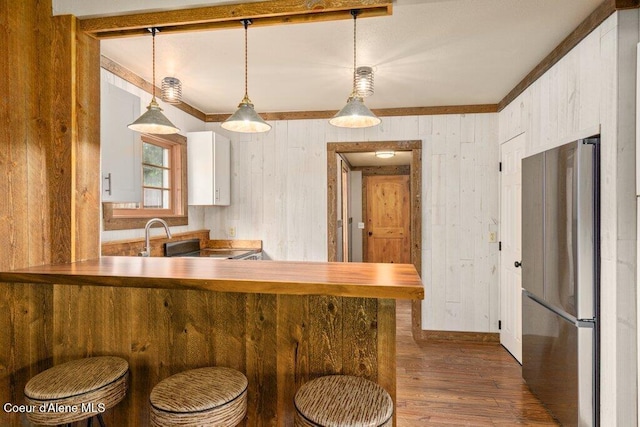707 Washington Ave, Sandpoint, ID 83864 - kitchen featuring freestanding refrigerator, dark wood-style flooring, wood walls, white cabinetry, and crown molding
