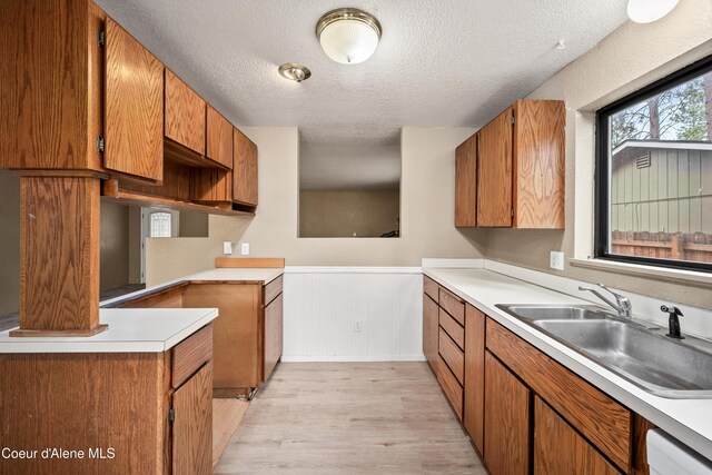 1706 E Thomas Ln, Coeur Dalene, ID 83815 - kitchen with a textured ceiling, a sink, light wood finished floors, a wainscoted wall, and brown cabinets