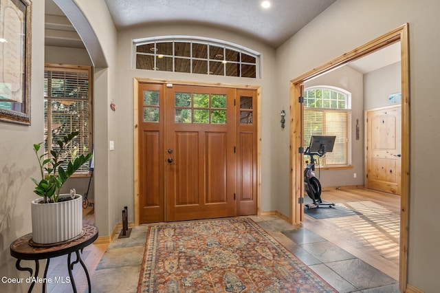 foyer entrance featuring baseboards, lofted ceiling, arched walkways, and stone tile flooring