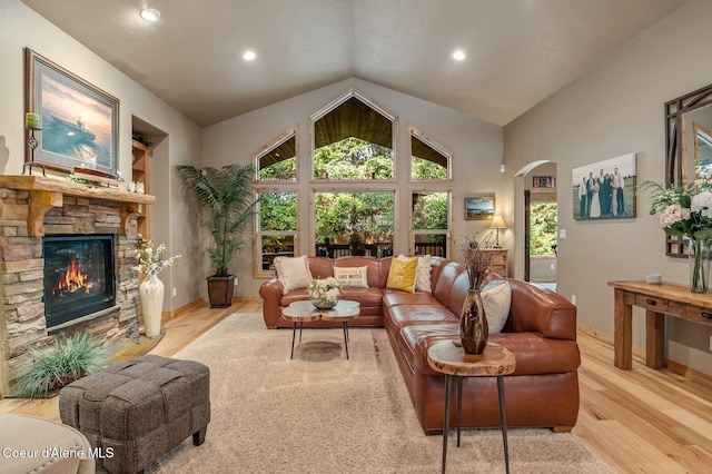 living area featuring wood finished floors, arched walkways, a stone fireplace, vaulted ceiling, and baseboards